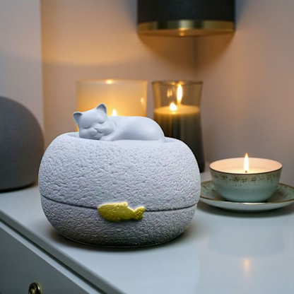 Grijze kattenurn: een vredig slapend poesje bovenop een ronde, steenachtige basis, met een subtiel gouden visje als detail