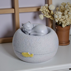 Grijze kattenurn: een vredig slapend poesje bovenop een ronde, steenachtige basis, met een subtiel gouden visje als detail