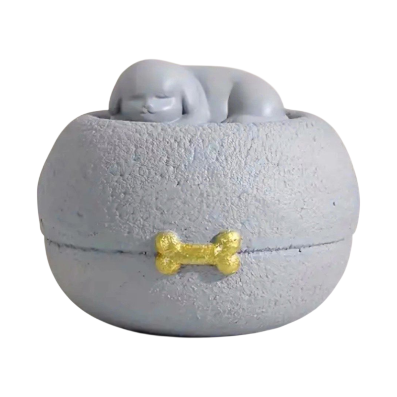 Grijze honden urn: een vredig slapend hondje bovenop een ronde, steenachtige basis, met een subtiel gouden botje als detail.