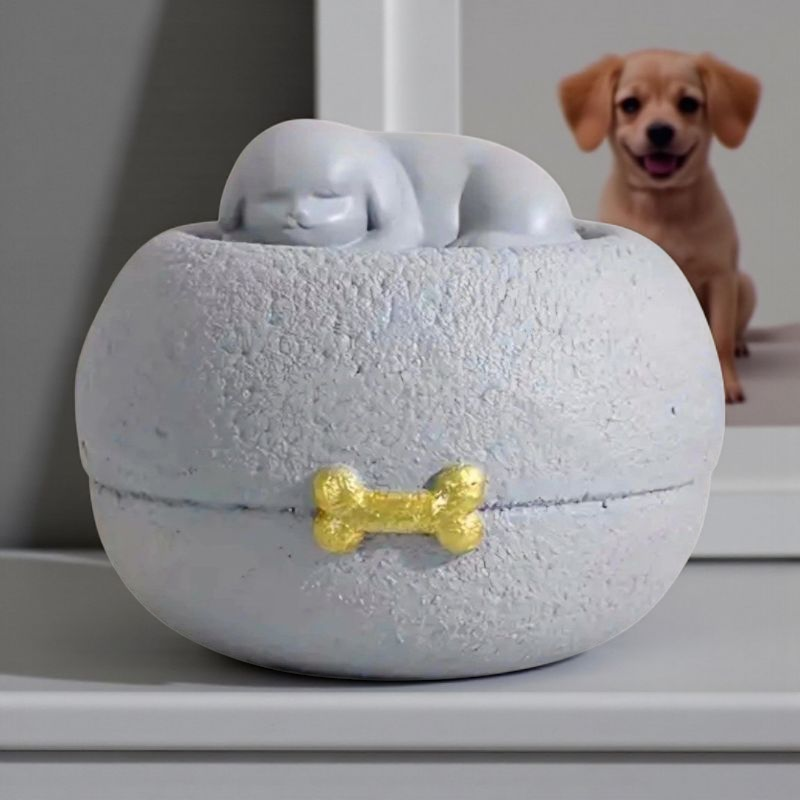 Grijze honden urn: een vredig slapend hondje bovenop een ronde, steenachtige basis, met een subtiel gouden botje als detail.